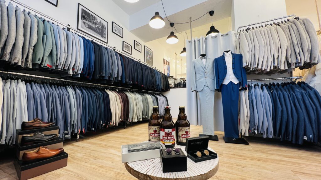 Hochzeitshaus Schubert – Brautmode & Hochzeitsanzüge 9 Herrenabteilung im Hochzeitshaus Schubert mit Hochzeitsanzügen an Kleiderstangen, zwei Anzügen an Puppen, Schuhen und Manschettenknöpfen